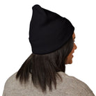A person with long dark hair wears the Printify Beanie Embroidered in black, paired with a beige sweater, shown from the back and slightly turned to the side.