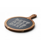 The Printify Charcuterie Board (Engraving) is a round acacia wood board with a handle and a dark slate center engraved with "BETTAVED DIST" in bold letters—an ideal personalized serving piece for any occasion.
